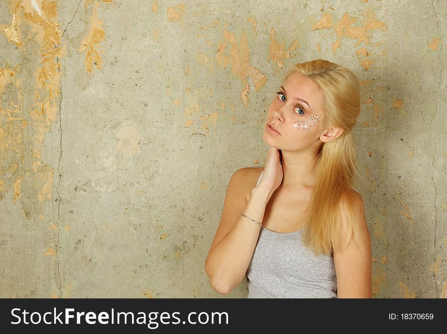 Beautiful young blond woman with makeup and multicolored crystals on the face. On the background of the old concrete. Beautiful young blond woman with makeup and multicolored crystals on the face. On the background of the old concrete