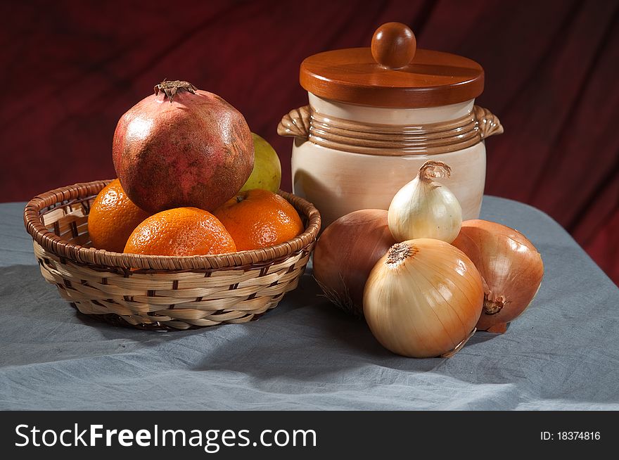 Onion, oranges, apple, basket and ceramic pot on a gray fabric. Onion, oranges, apple, basket and ceramic pot on a gray fabric.