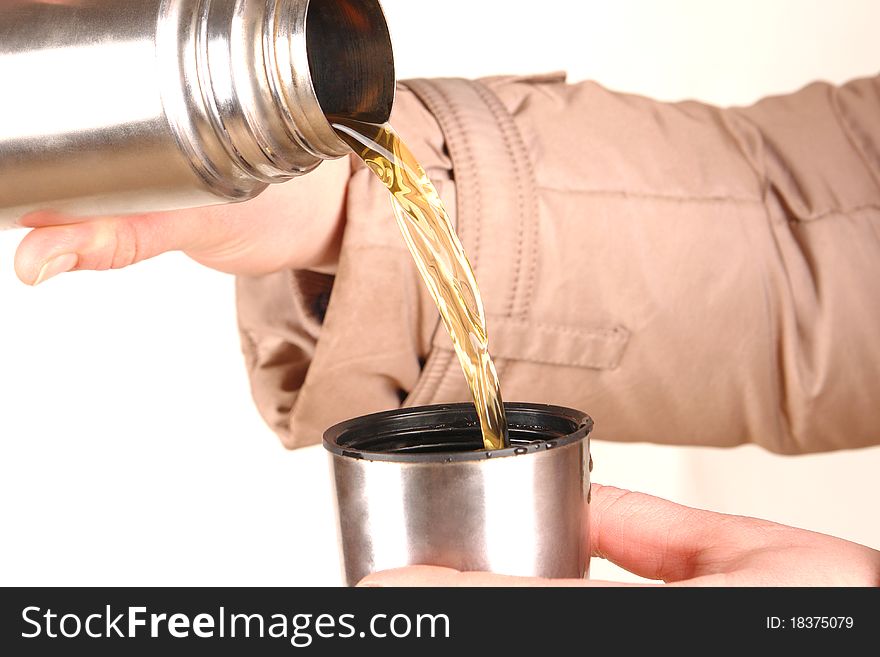 Thermos in a hand, pouring tea into a cup.