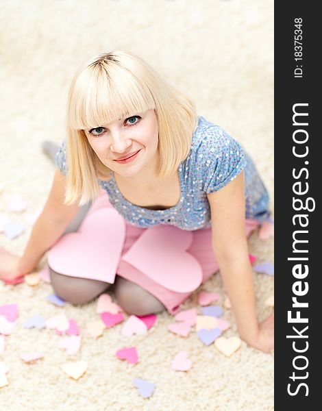 Beautiful young adult sitting on the floor and a lot of paper hearts are around her