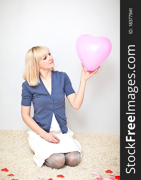 Beautiful young adult holding big heart in her hand sitting on the floor
