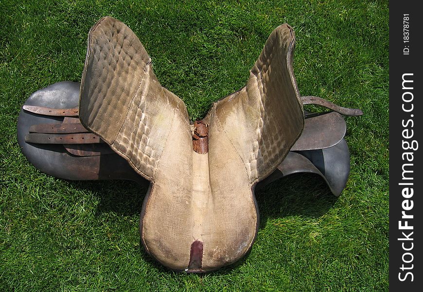 Very old English horse saddle on grass taken from the bottom side. Very old English horse saddle on grass taken from the bottom side