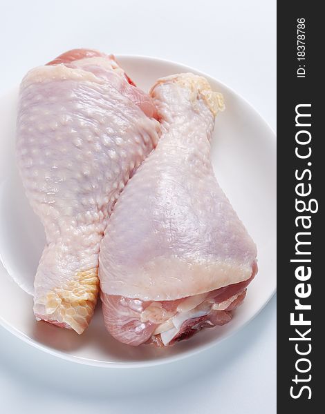 Two raw chicken legs on a plate on a white background