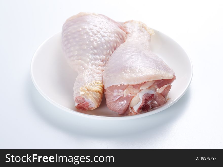 Two raw chicken legs on a plate on a white background