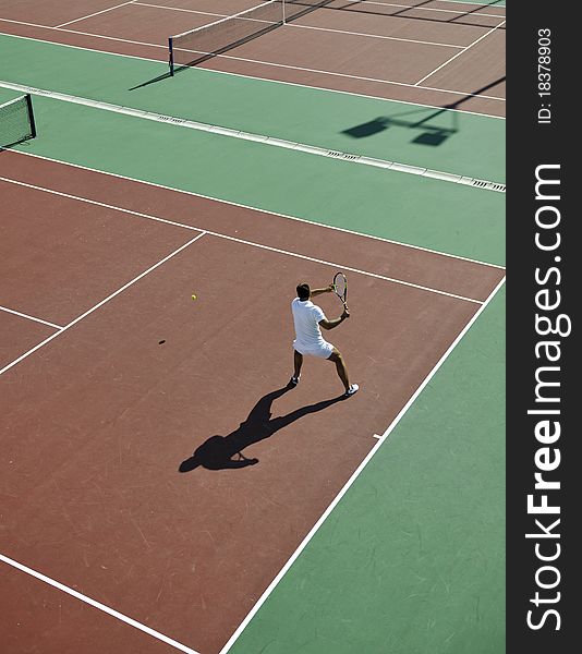 Young man play tennis outdoor on orange tennis field at early morning