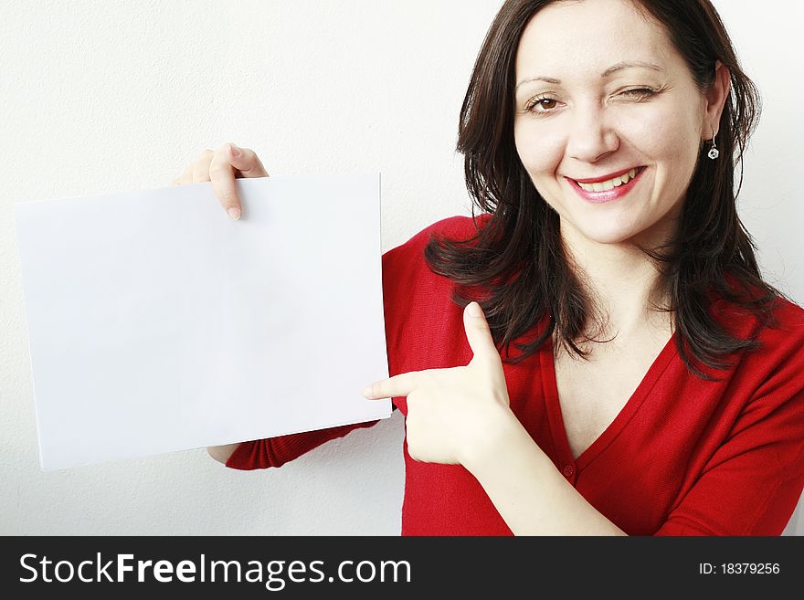 Young woman smiling, winking, pointing at a blank paper. Young woman smiling, winking, pointing at a blank paper