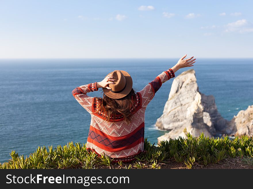 Closeup back view of woman in travel clothes and hat sitting and looking at blue ocean and sky. Travel concept photo