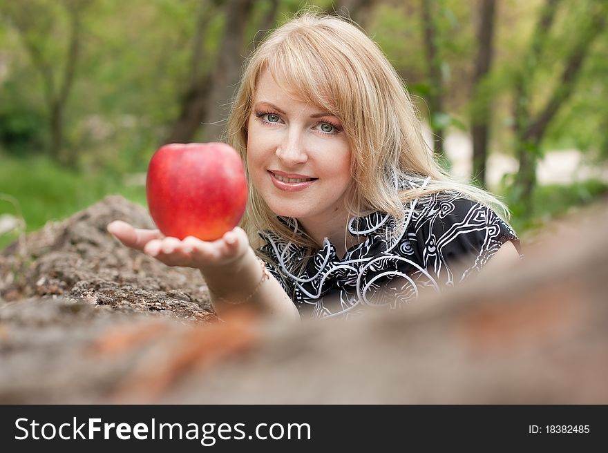 Beautiful smiling young woman with red apple in her hand outdoors, spring day