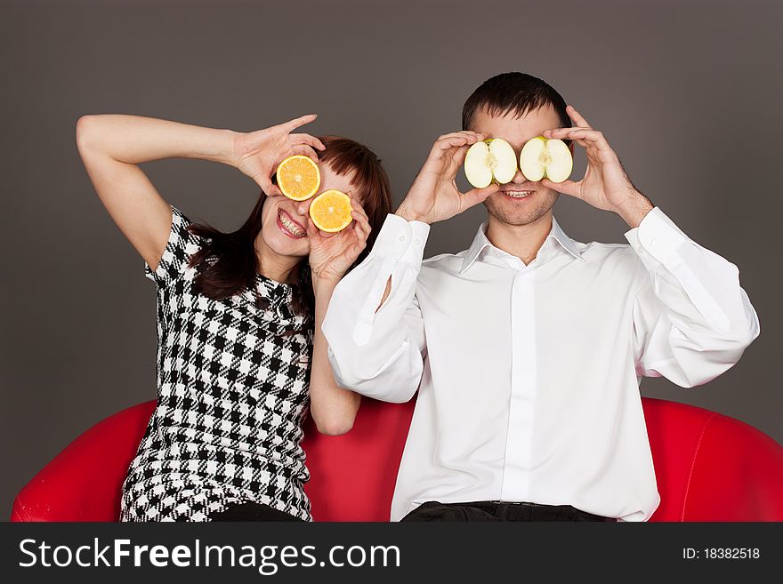 Funny couple shutting eyes with apple and orange in studio against gray