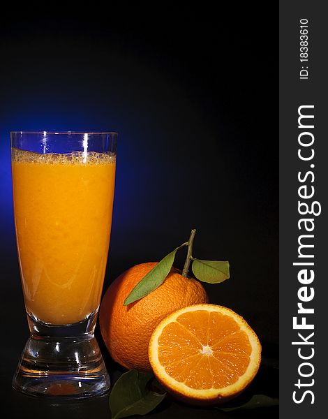 Natural orange juice in a glass and orange fruit, on black background shooting with blue gel. Natural orange juice in a glass and orange fruit, on black background shooting with blue gel