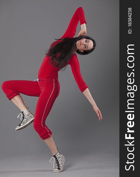 Dancing woman in red sport suit over grey background