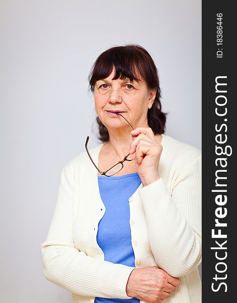 Senior woman standing at the wall holding her glasses and looking into the camera. Senior woman standing at the wall holding her glasses and looking into the camera