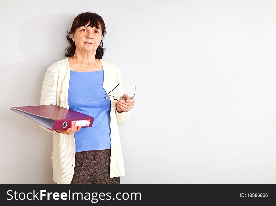 Good looking senior woman with folder and glasses standing at the wall and looking into the camera. Good looking senior woman with folder and glasses standing at the wall and looking into the camera