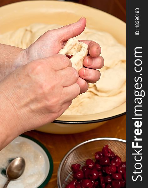 Female hands making small pies with cherry on a table. Female hands making small pies with cherry on a table