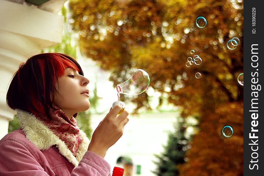 A girl is in an autumn park blowing a soap-bubbles