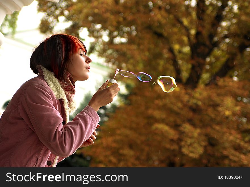 A girl is in an autumn park blowing a soap-bubbles