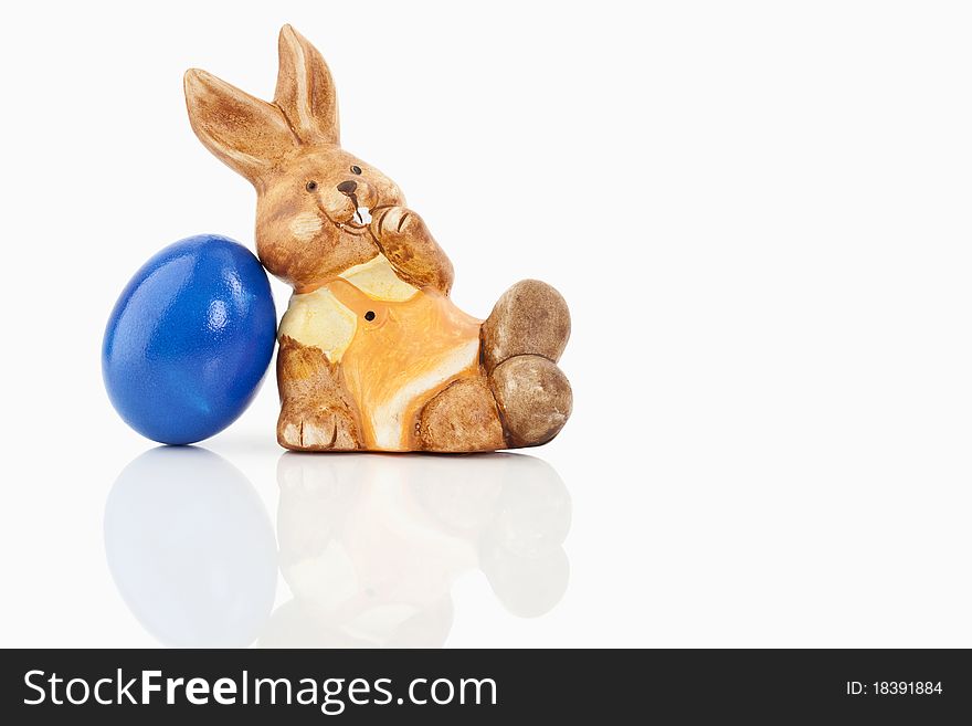 Easter bunny sitting close to a blue egg on a white background