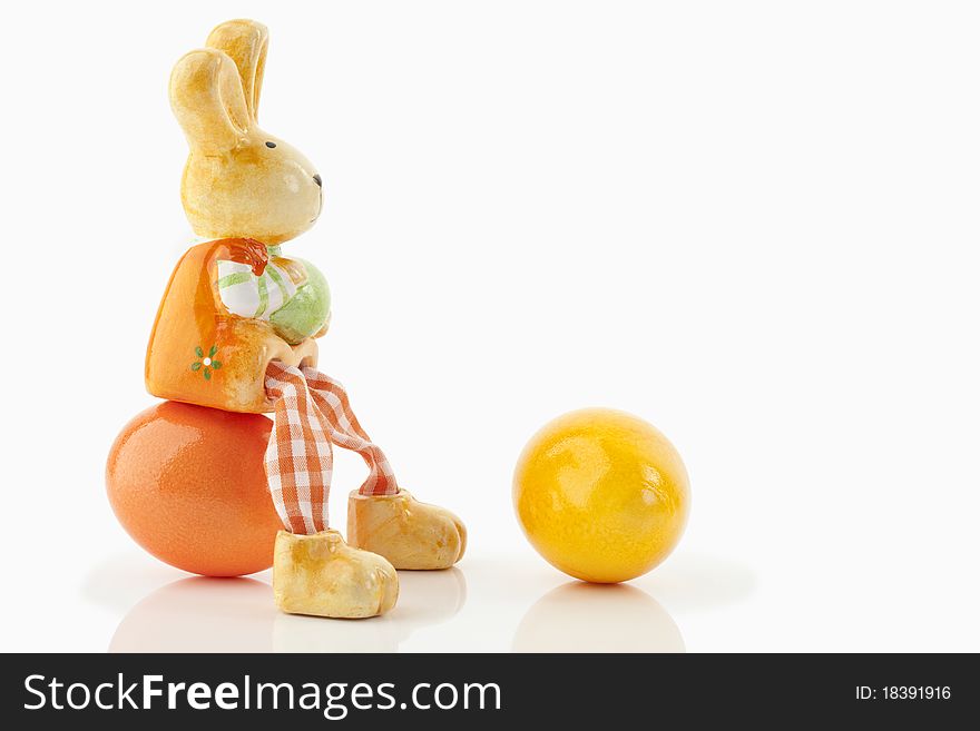 Easter bunny sitting on an orange egg close to a yellow egg on a white background