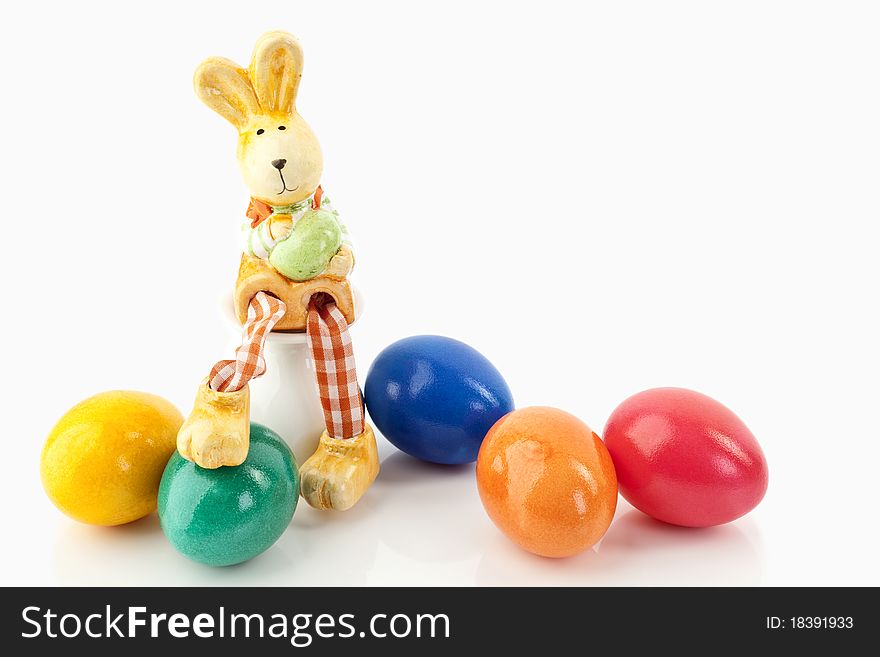 Easter bunny sitting on an egg-cup close to colored eggs on a white background