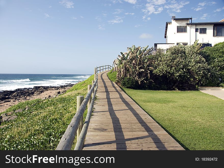 A wooden walkway with a handrail next to a bech. A wooden walkway with a handrail next to a bech