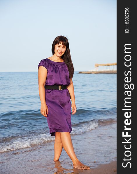 Young woman in dress standing on sand on sea background