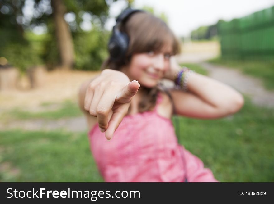 Beautiful teenage girl in a pink dress with headphones to point the finger at the camera, focus on finger. Beautiful teenage girl in a pink dress with headphones to point the finger at the camera, focus on finger