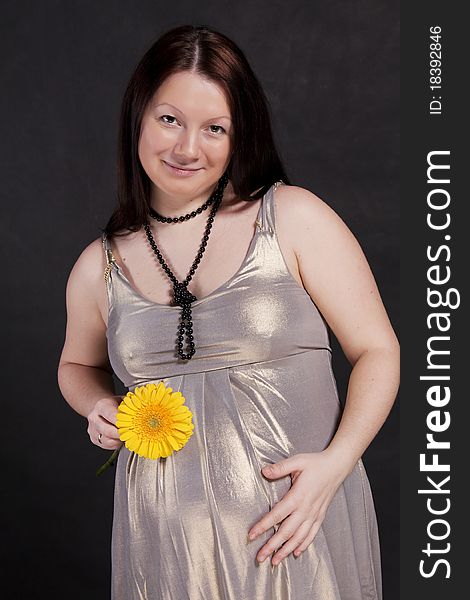 A smiling pregnant woman in a dress with a flower gerbera