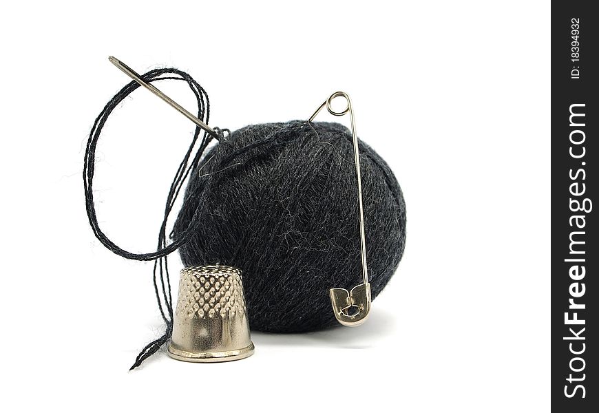 Black thread ball, pin, thimble and needle on a white background