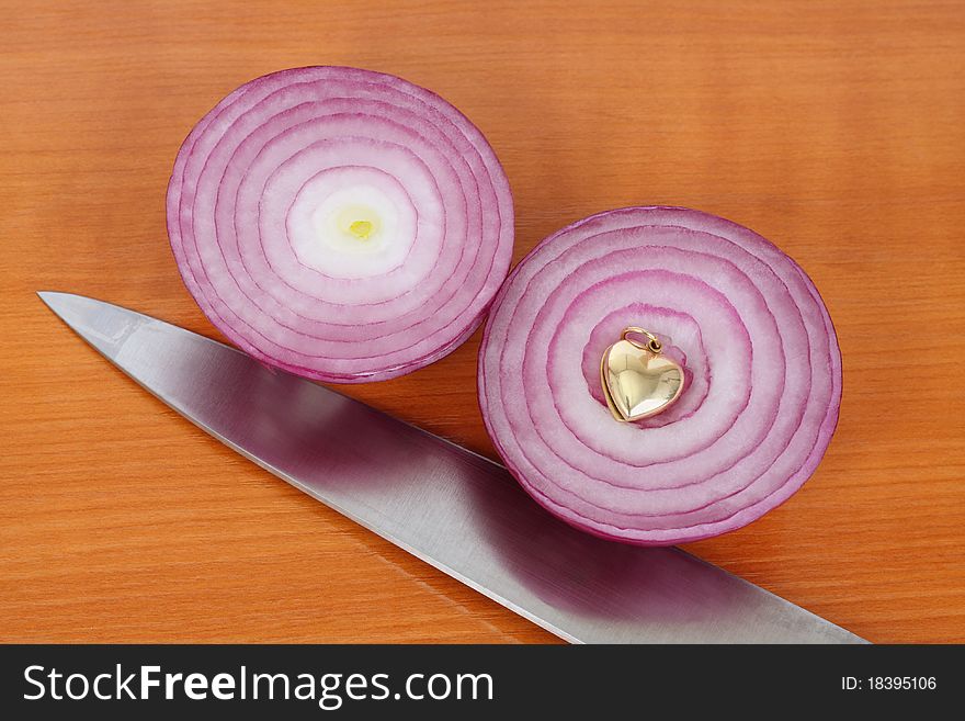 Two red onion halves, kitchen knife and golden heart on the kitchen board. Two red onion halves, kitchen knife and golden heart on the kitchen board