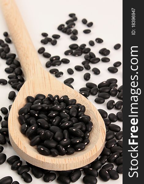 Black beans with a wooden spoon on white background