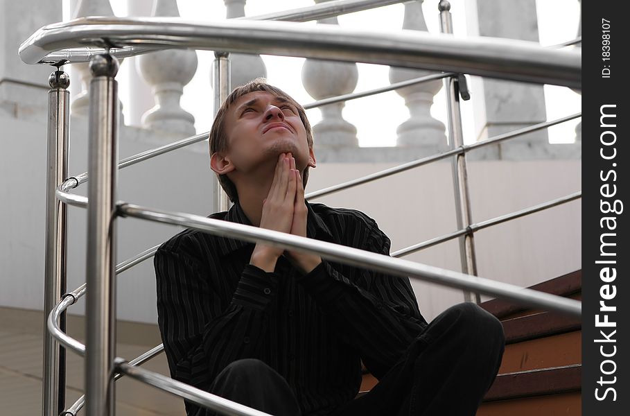 A young man in a black shirt sitting on the stairs and asks for help sky