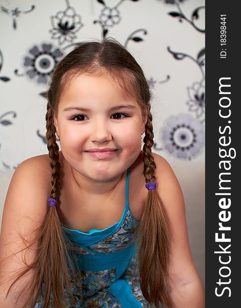 A smiling little girl in a blue dress and pigtails on the head.