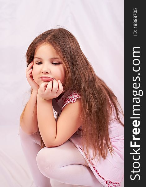 A girl sits upset and thinking about pressing issues on a white background, white tights and white-pink dress. A girl sits upset and thinking about pressing issues on a white background, white tights and white-pink dress.