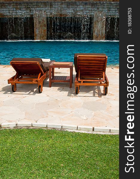 A portrait of tropical swimming pool setup with chairs, towers, greenery and waterfall