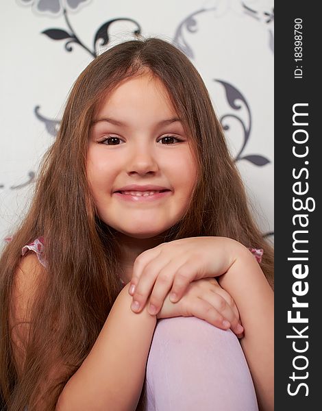 The little girl is sitting, smiling, his hands placed on the knee. The little girl is sitting, smiling, his hands placed on the knee.