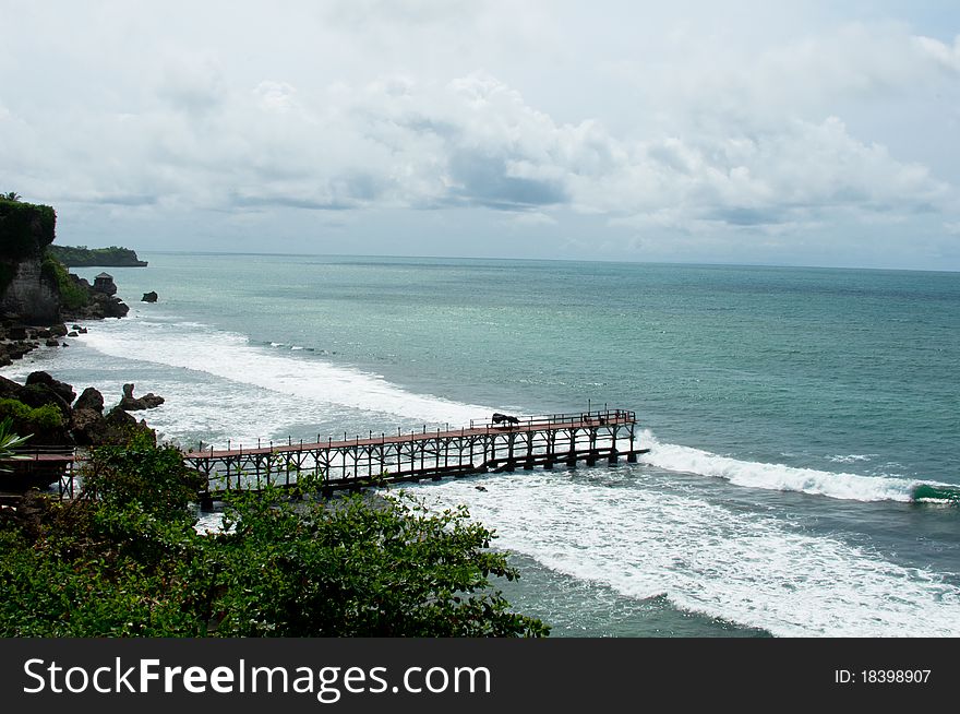 An aerial view of a wooden jetty in Bali overseeing Indian ocean with a cloudy sky. An aerial view of a wooden jetty in Bali overseeing Indian ocean with a cloudy sky