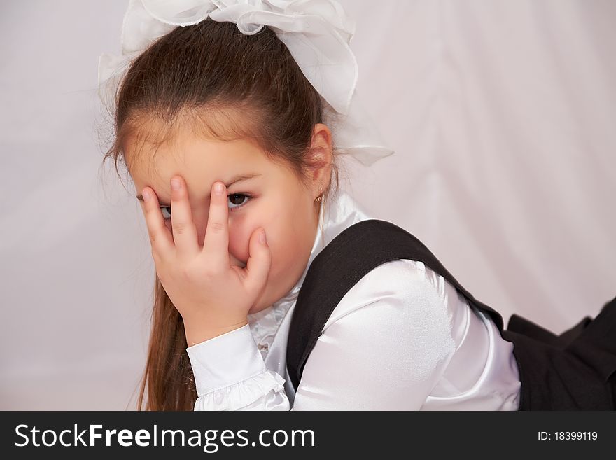 The little girl in school uniform lying and covers his face with his fingers. The little girl in school uniform lying and covers his face with his fingers.
