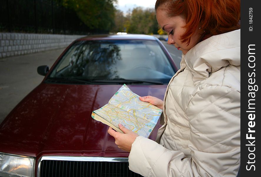 The young girl with a map of streets on a background of the red automobile