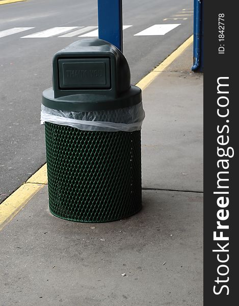 A Green Trash can on the side of a pavement