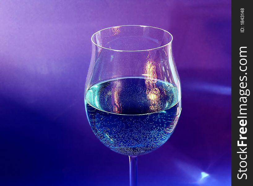 One glass with a drink and a reflection of a near fireplace on blue background. One glass with a drink and a reflection of a near fireplace on blue background