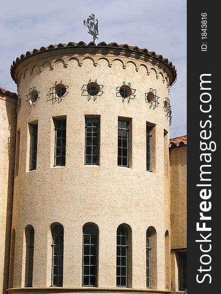 Round portion of Mediterrarean building with weathervane and unusual windows: round, tall rectangular and tall arched. Round portion of Mediterrarean building with weathervane and unusual windows: round, tall rectangular and tall arched