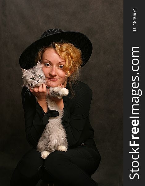 The beautiful girl in a black hat covers a kitten. The beautiful girl in a black hat covers a kitten