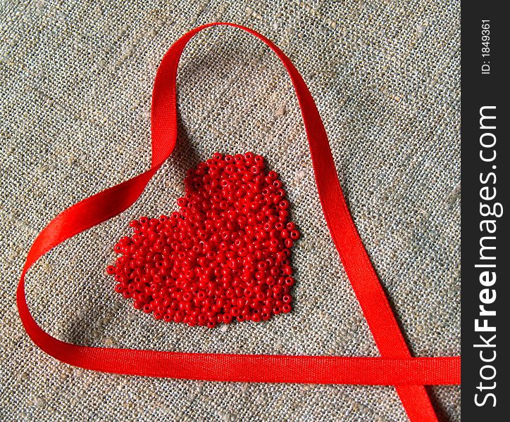 Scarlet ribbon and beads heart on the canvas. Scarlet ribbon and beads heart on the canvas