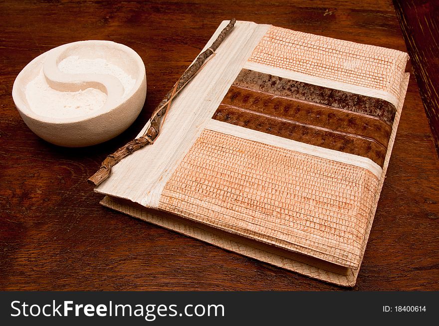 An artistic design of book made with natural wooden material with yin and yang sand bowl on a wooden table. An artistic design of book made with natural wooden material with yin and yang sand bowl on a wooden table