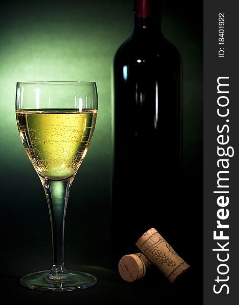 Crystal wine glass with white wine and a bottle, on black background with green gel, Luxury art background for beverages (part of collection)