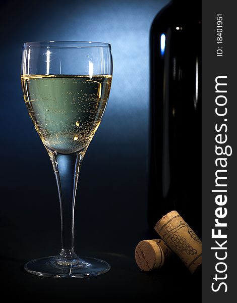 White wine in a glass closeup & a bottle, on black-blue background. Art heme. White wine in a glass closeup & a bottle, on black-blue background. Art heme