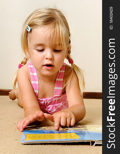 Young adorable blonde girl reads a book on her own. Young adorable blonde girl reads a book on her own