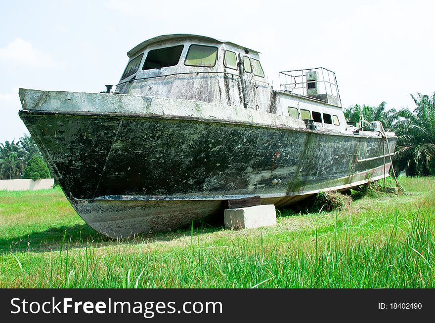 An old abandoned wooden boat on a grass field with palm at the background. An old abandoned wooden boat on a grass field with palm at the background