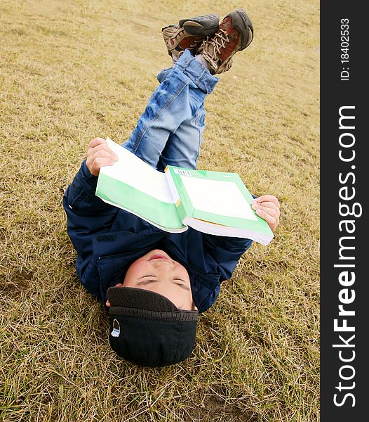 Picture of a little chinese boy reading a book while lying on the garden lawn in the spring sunshine. Picture of a little chinese boy reading a book while lying on the garden lawn in the spring sunshine