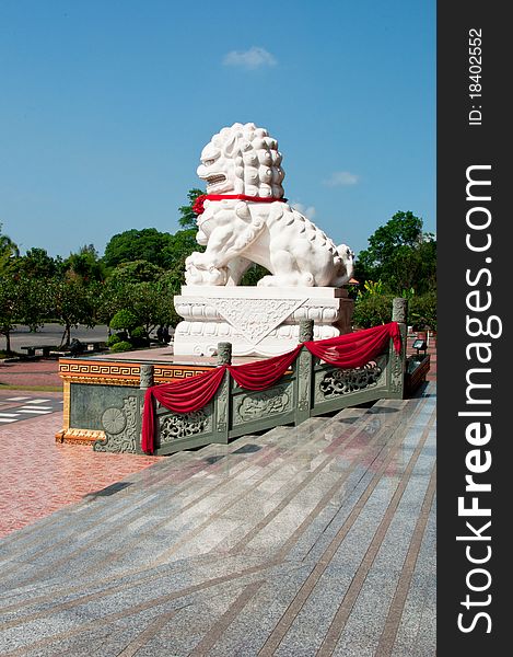 A stone lion outside the temple with a foreground of marble steps and a lush greenery at the background. A stone lion outside the temple with a foreground of marble steps and a lush greenery at the background